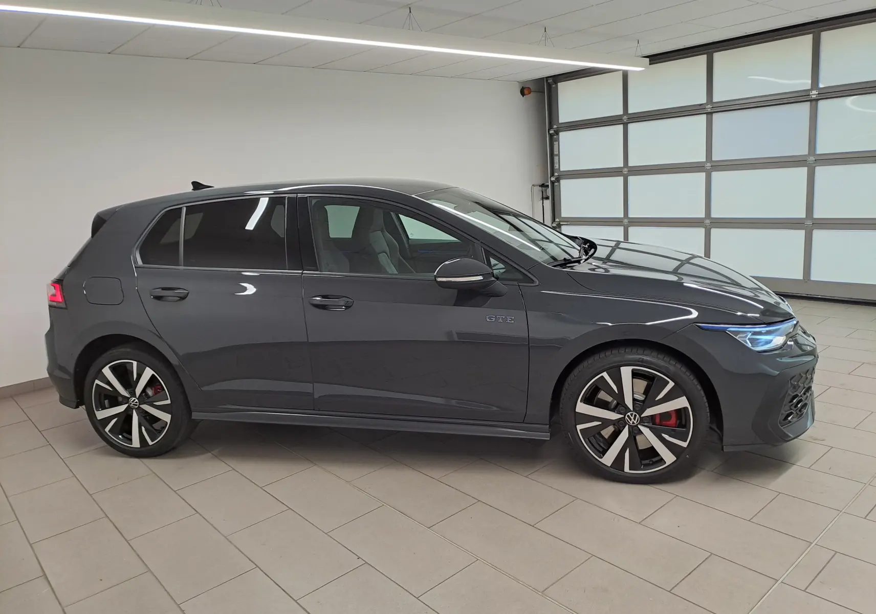 Volkswagen Golf 1.5 eHybrid 272 DSG6 GTE gris Urano vue de profil côté gauche en intérieur, avec jantes distinctives et logo GTE.
