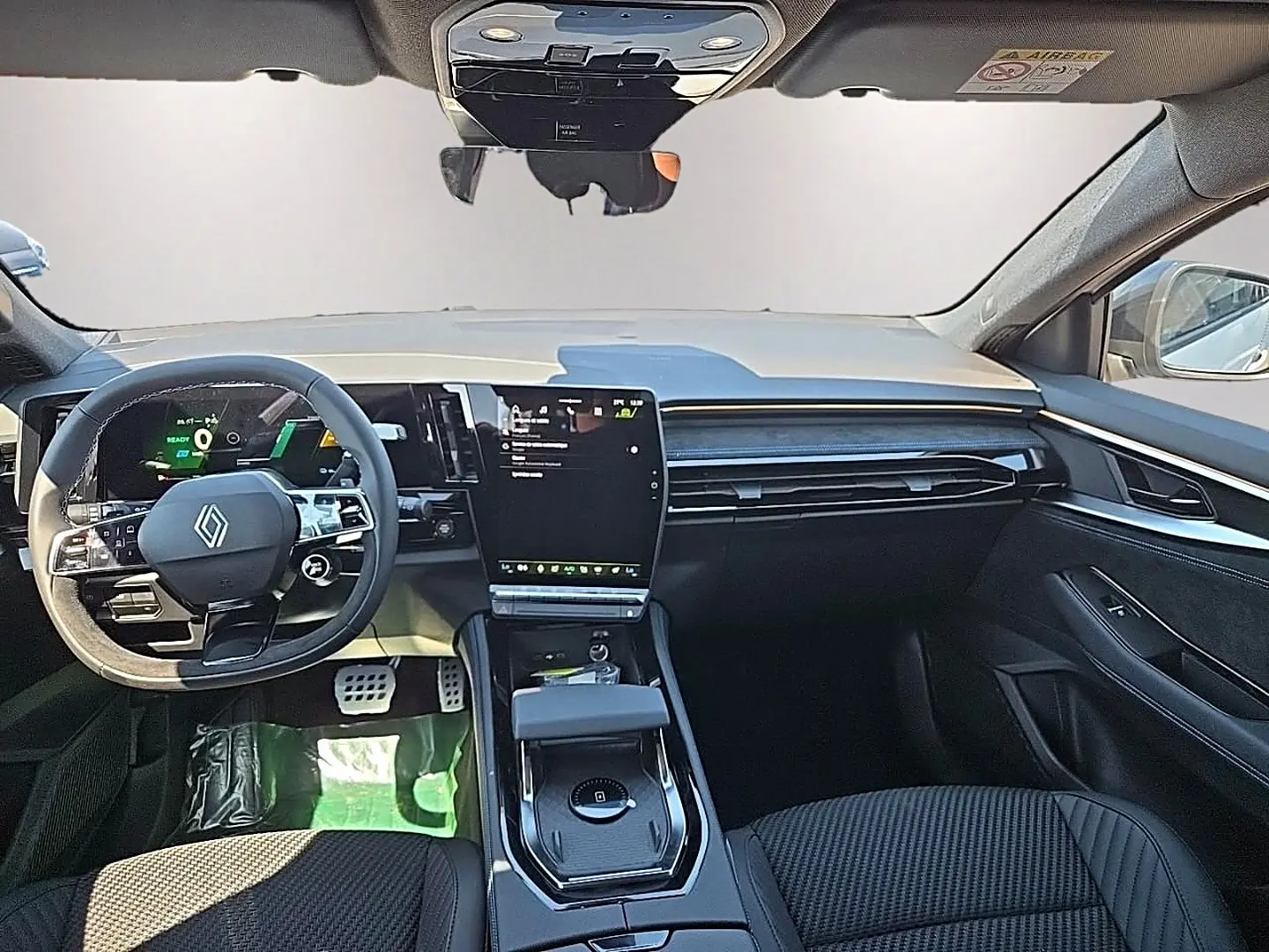 Vue avant de l’intérieur noir du Renault Austral blanc nacré, avec volant multifonction et écran tactile central vertical.