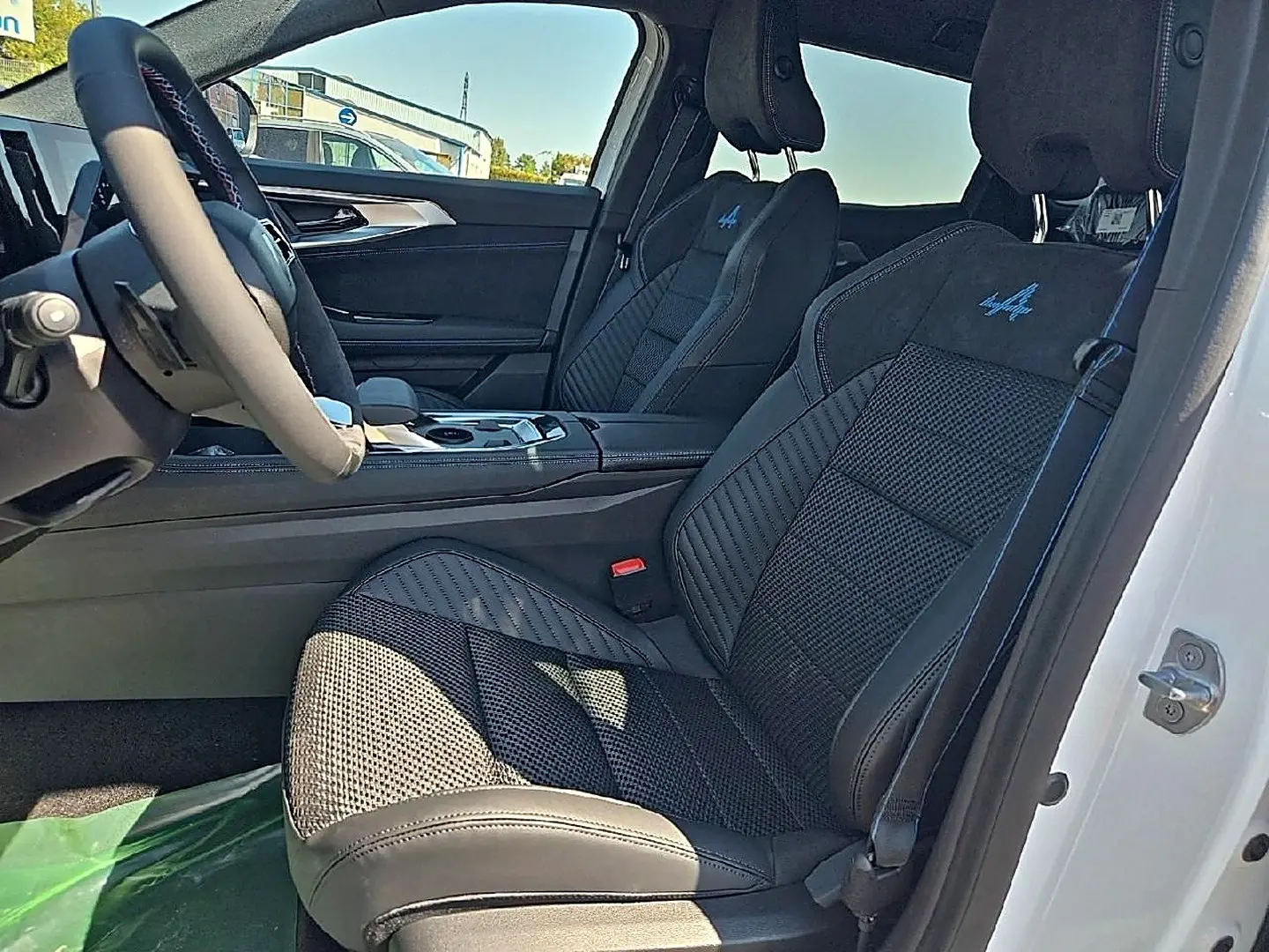 Vue intérieure côté conducteur du Renault Austral blanc nacré, sièges sport noirs avec logo Alpine bleu brodé.