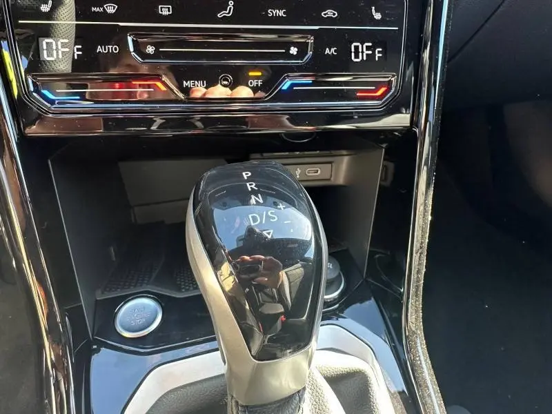 Gros plan sur la commande de boîte automatique noire du Volkswagen T-Roc 2025, avec console brillante et commandes climatisation.