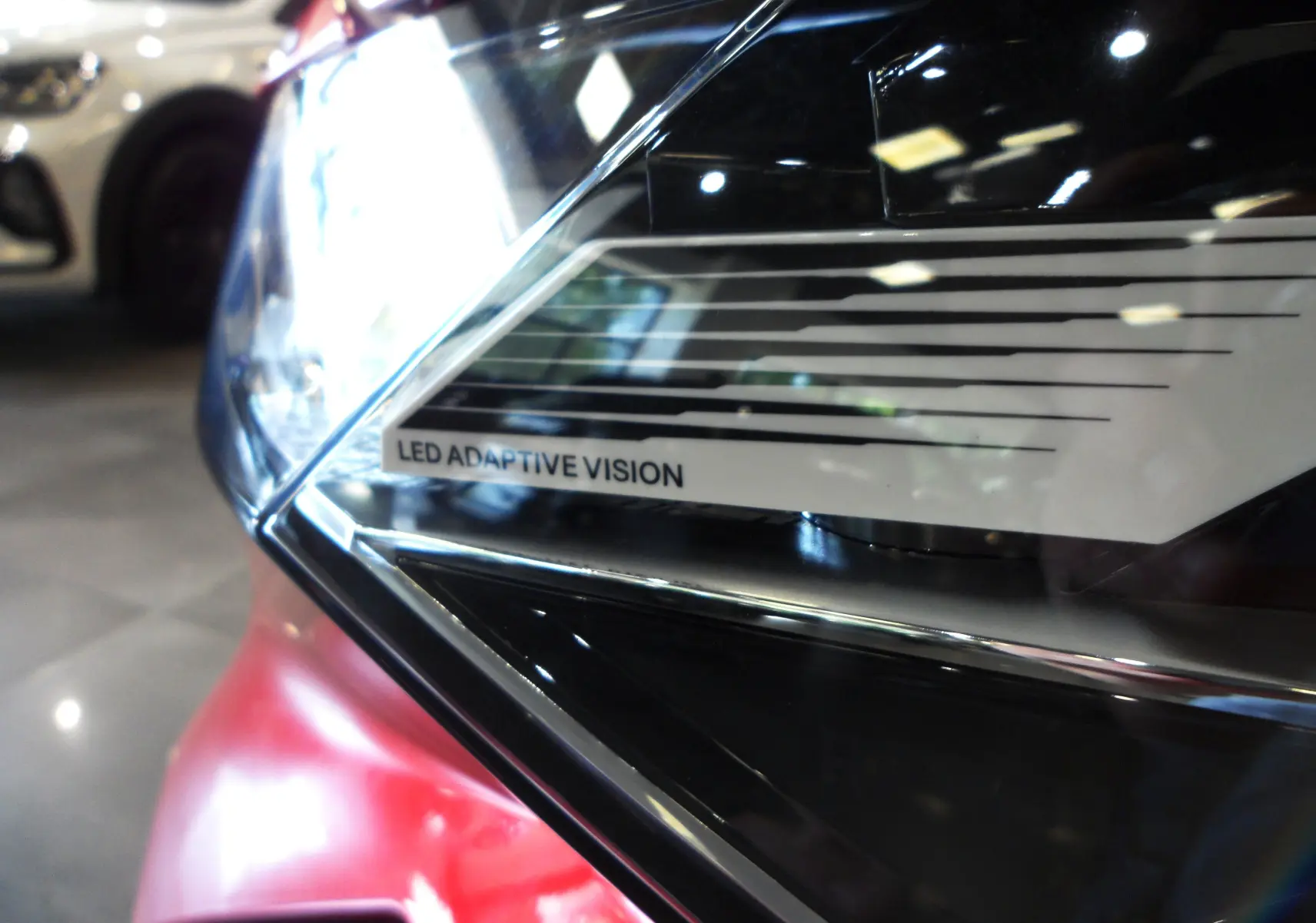 Gros plan sur le phare avant gauche rouge flamme de la Renault Rafale 2025 avec inscription LED Adaptive Vision.