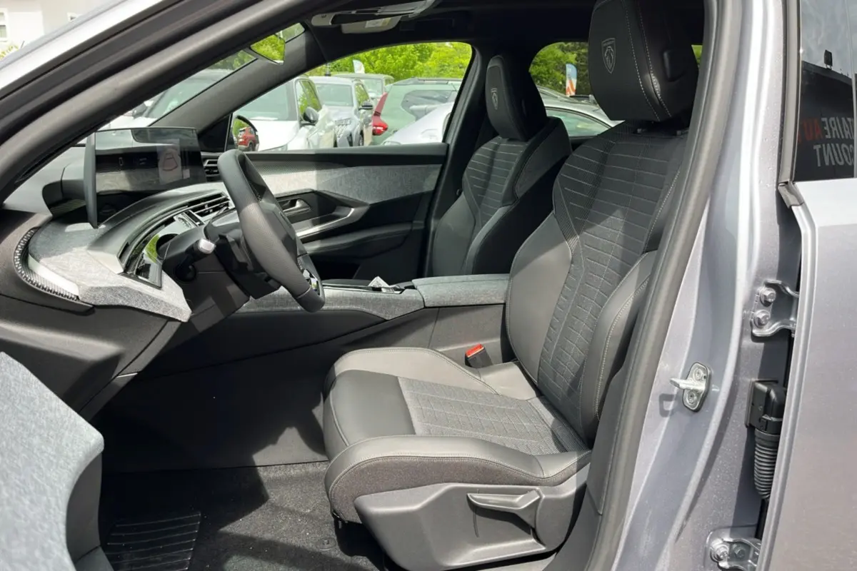 Vue intérieure côté conducteur du Peugeot 3008 Hybrid 2025 gris titane, sièges en tissu et cuir avec logo Peugeot brodé.