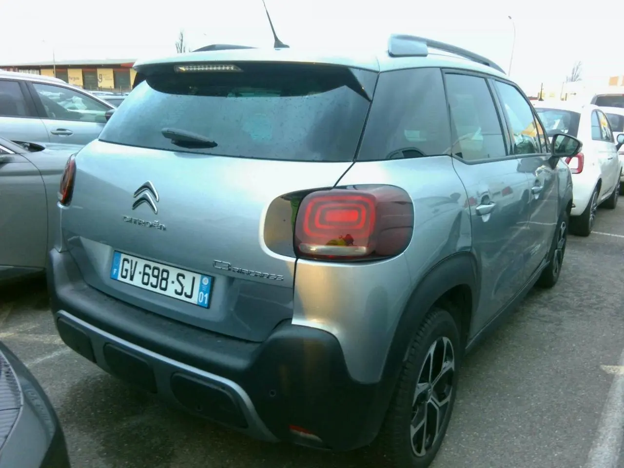 Vue 3/4 arrière droite d'une Citroën C3 Aircross gris foncé avec jantes alliage et barres de toit noires.