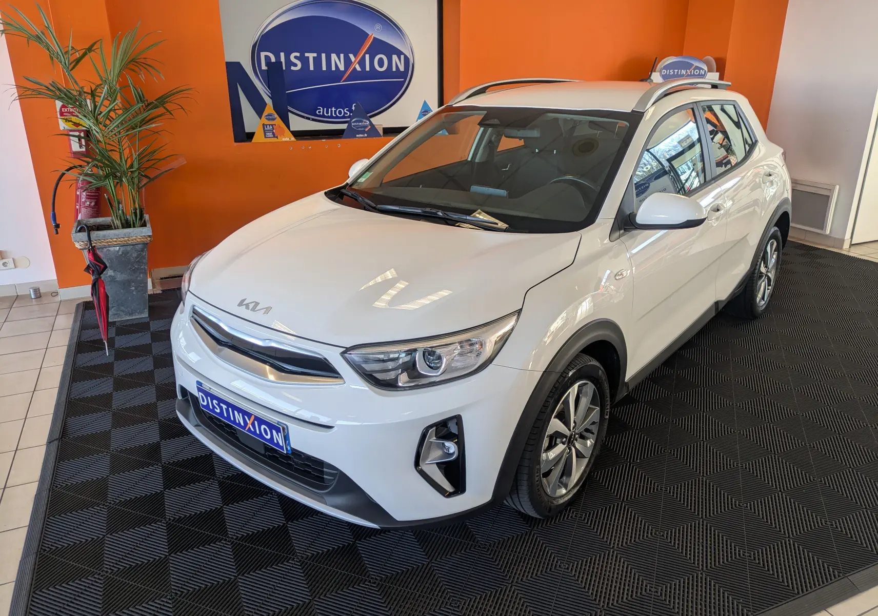 KIA Stonic blanc en 3/4 avant droit dans un showroom avec logo Distinxion en arrière-plan.