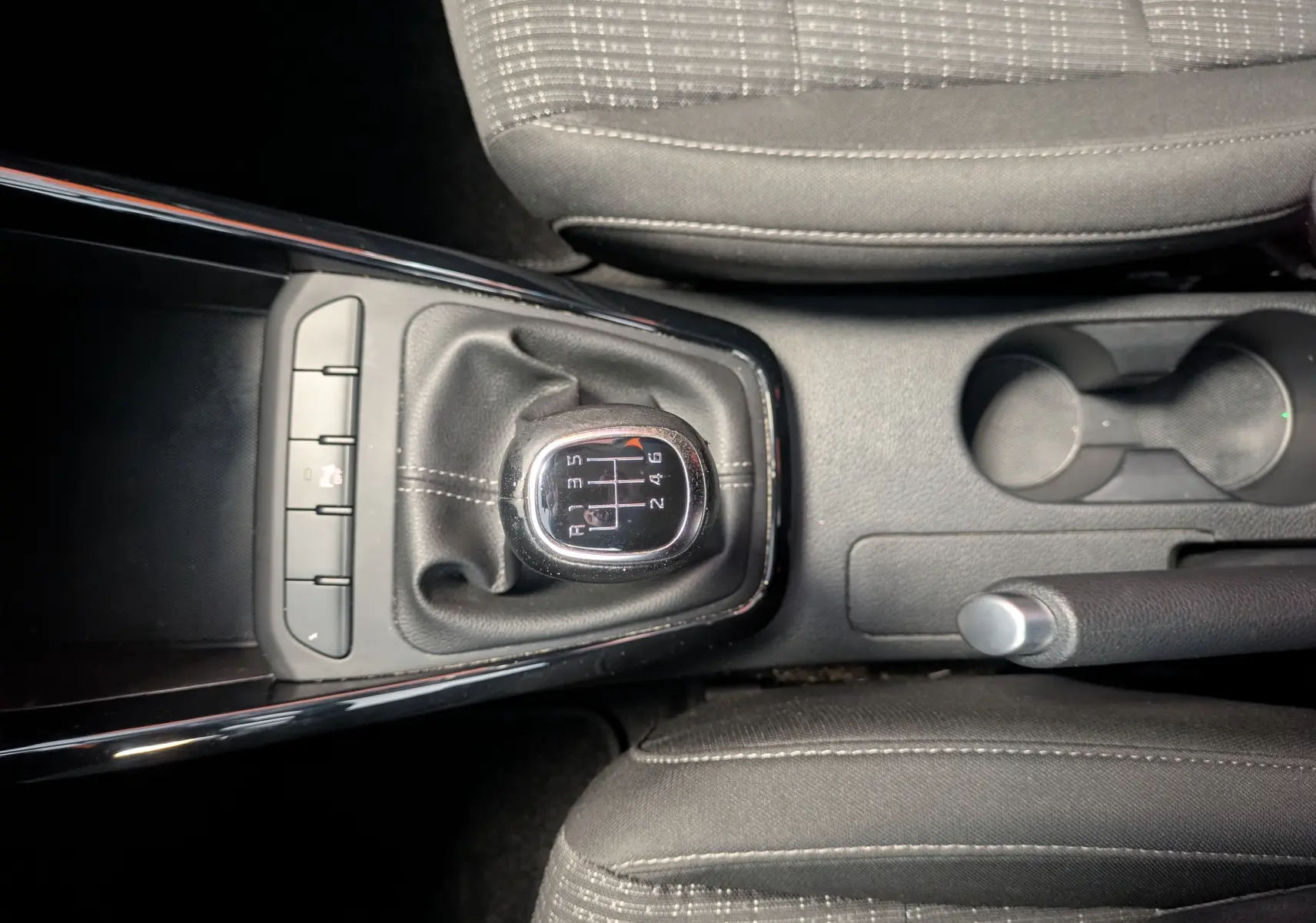 Vue de dessus du levier de vitesses manuel noir et gris entouré de sièges tissu gris dans une KIA Stonic blanche de 2022.