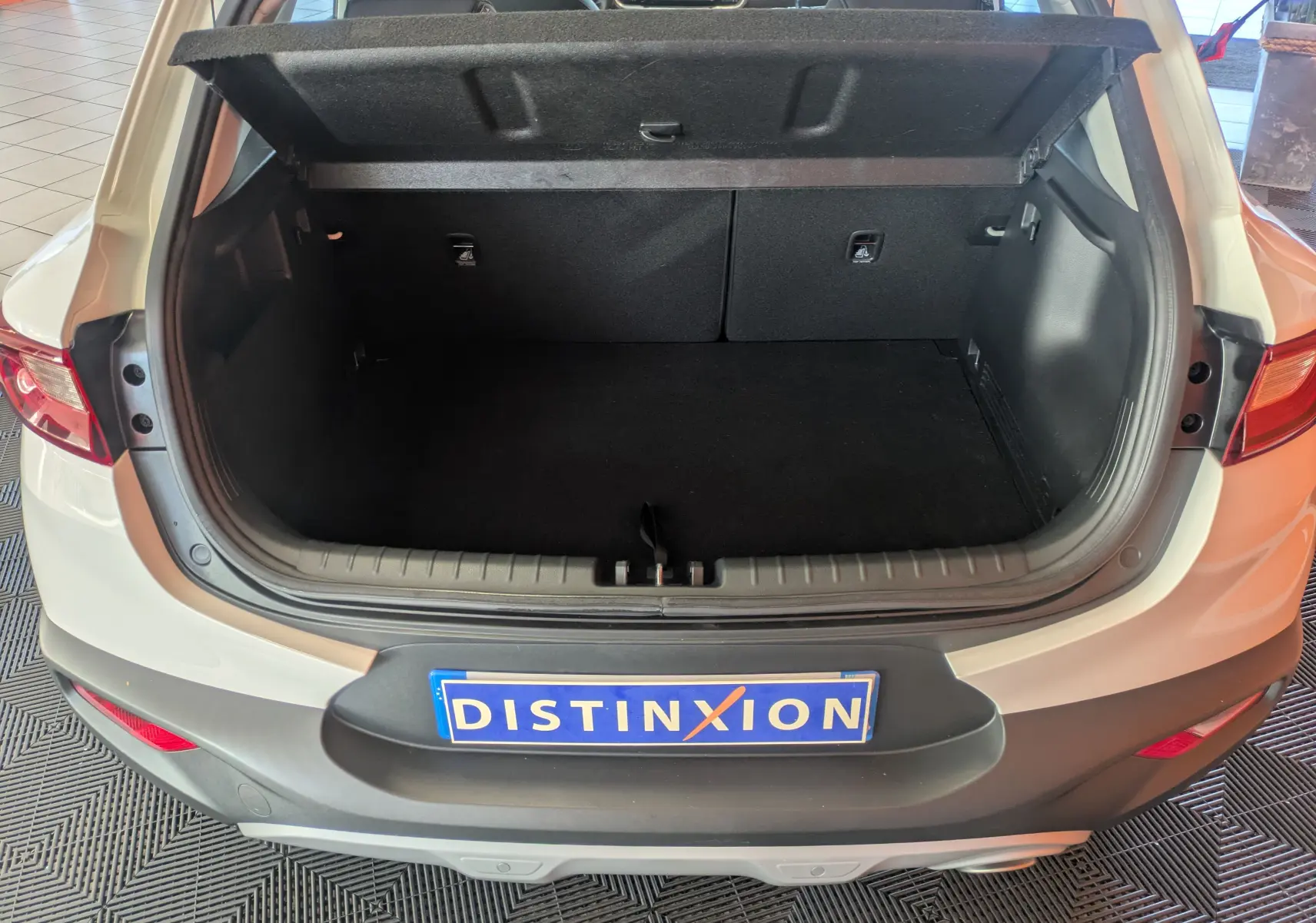 Coffre ouvert vu de l'arrière d'un KIA Stonic blanc 2022, montrant l'espace de chargement et la tablette cache-bagages relevée.
