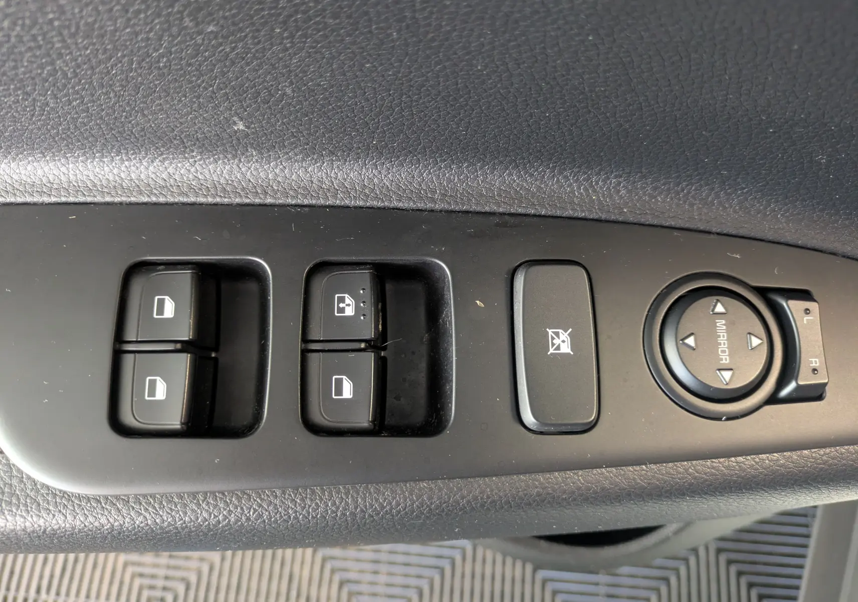 Gros plan sur les commandes de lève-vitres et réglage des rétroviseurs côté conducteur d’un KIA Stonic blanc.