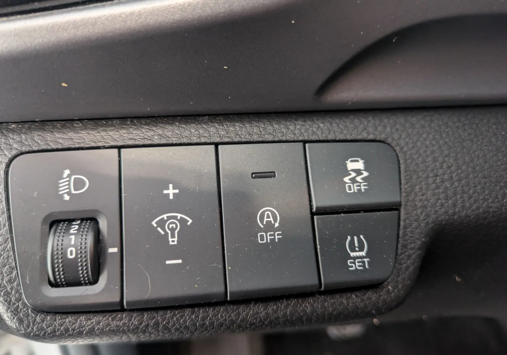 Gros plan sur les commandes noires du tableau de bord du Kia Stonic blanc, avec réglage phares et fonctions de sécurité.