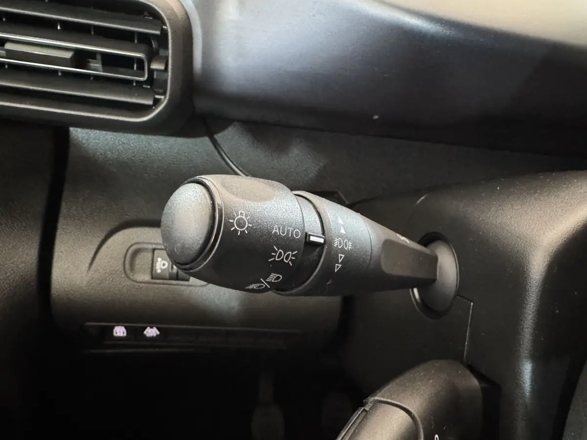 Gros plan sur la commande des feux à gauche du volant dans l’habitacle noir du Peugeot Rifter blanc 2019.