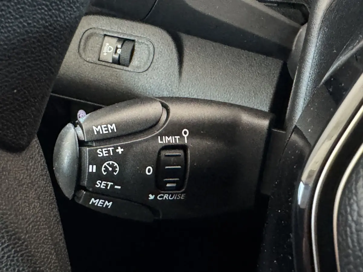 Gros plan sur la commande de régulateur et limiteur de vitesse noire dans l'habitacle du Peugeot Rifter blanc.