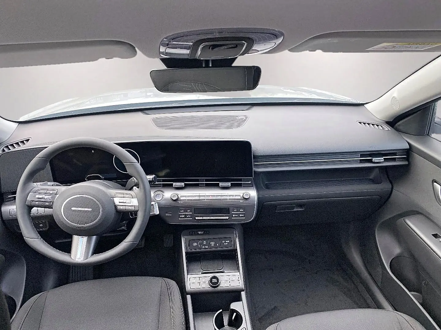 Vue intérieure avant du Hyundai Kona gris 2025, tableau de bord moderne avec écran large et volant multifonction cuir.
