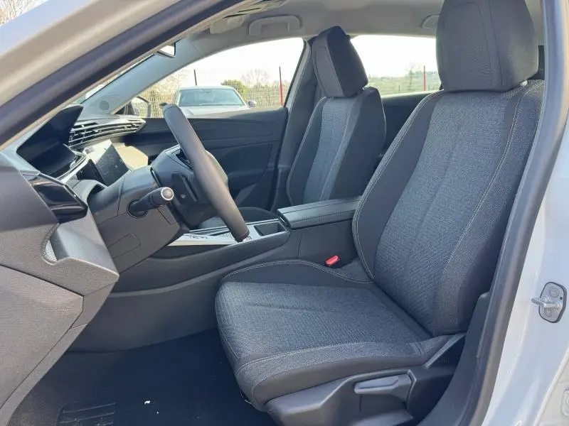 Vue intérieure côté conducteur de la Peugeot 308 blanche Okénite, sièges tissu gris avec accoudoir central.
