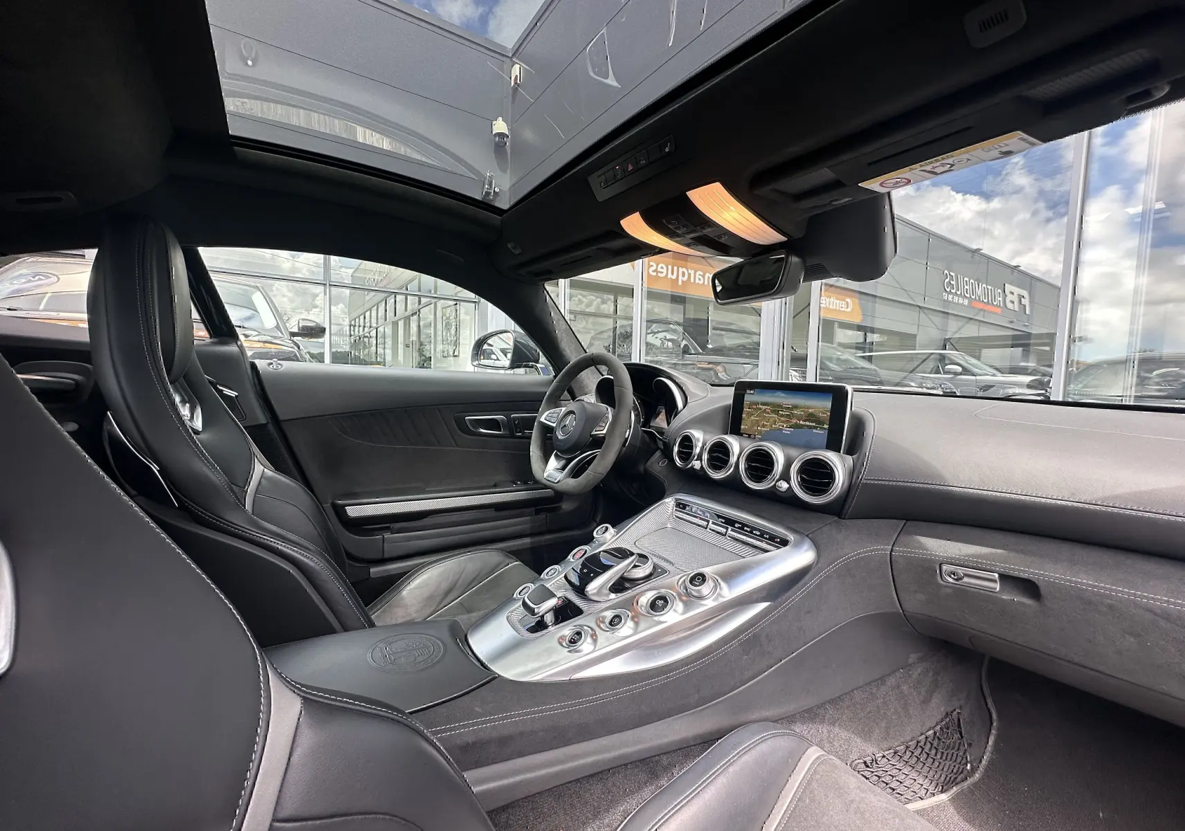 Vue intérieure côté conducteur du Mercedes AMG GT 2015 gris foncé, avec console centrale alu et toit panoramique.