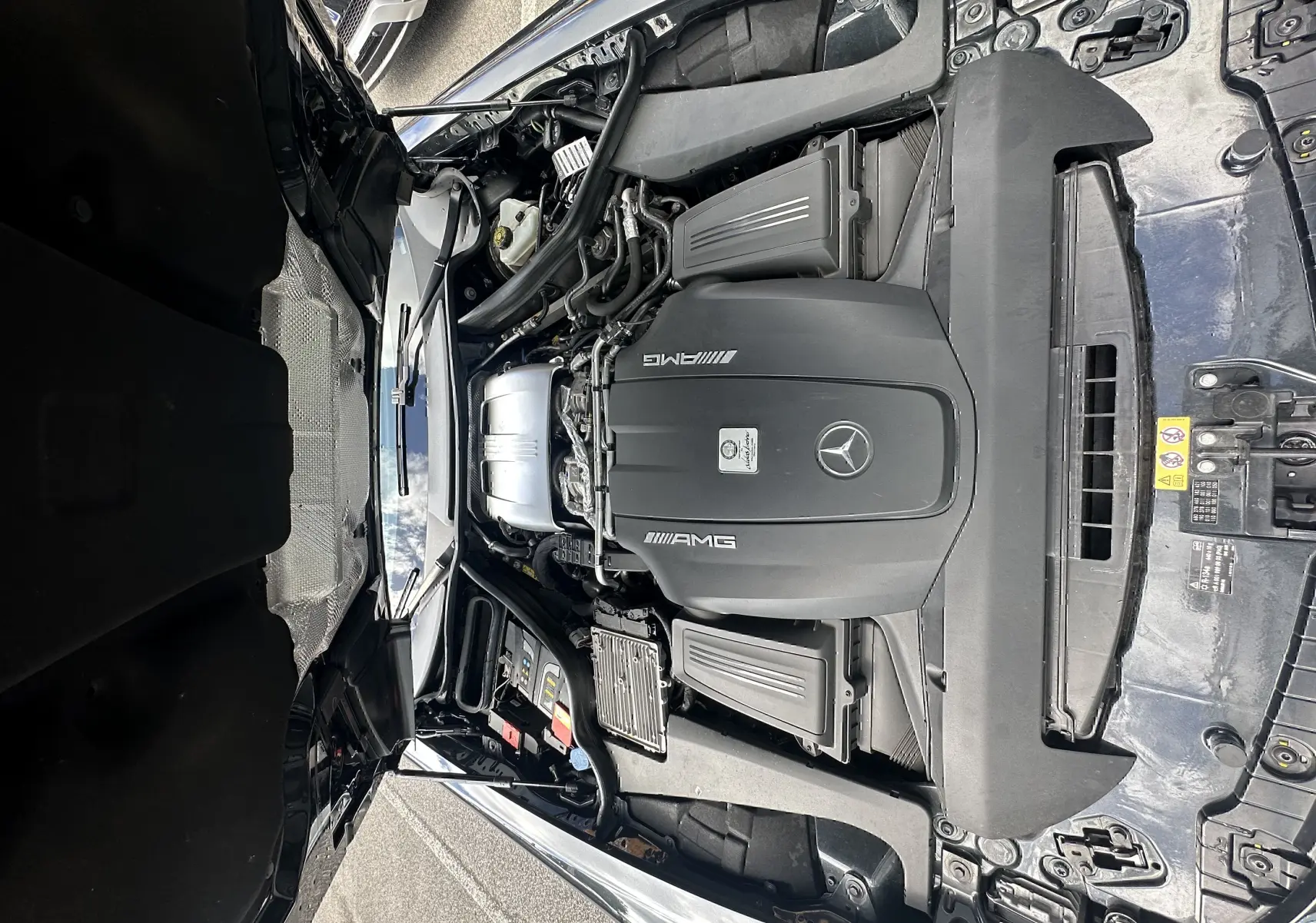 Moteur AMG V8 visible sous le capot ouvert d'une Mercedes AMG GT gris foncé, vue de dessus en extérieur.