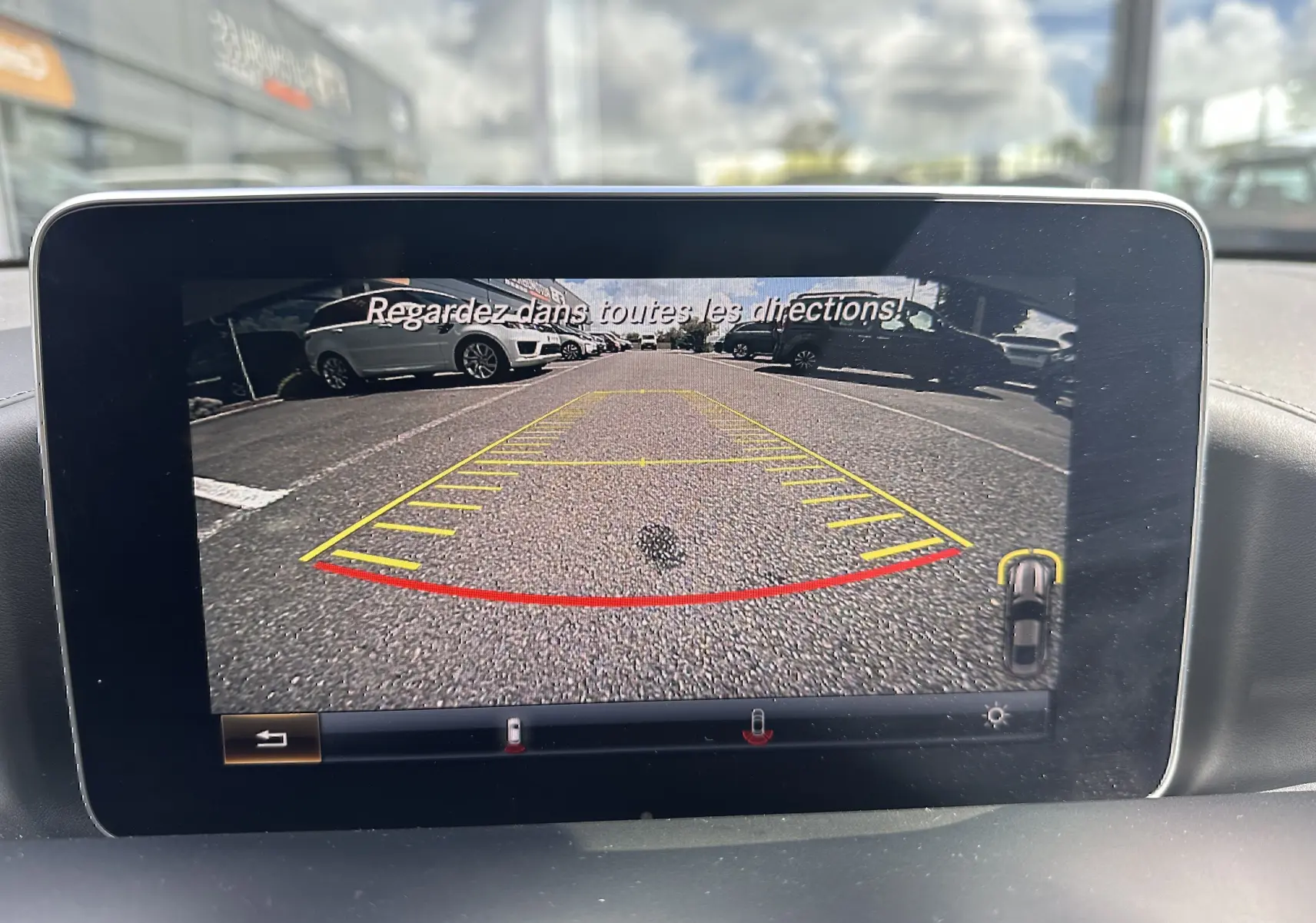 Vue arrière depuis la caméra de recul d'une Mercedes AMG GT gris foncé, avec les lignes de guidage visibles sur l'écran.