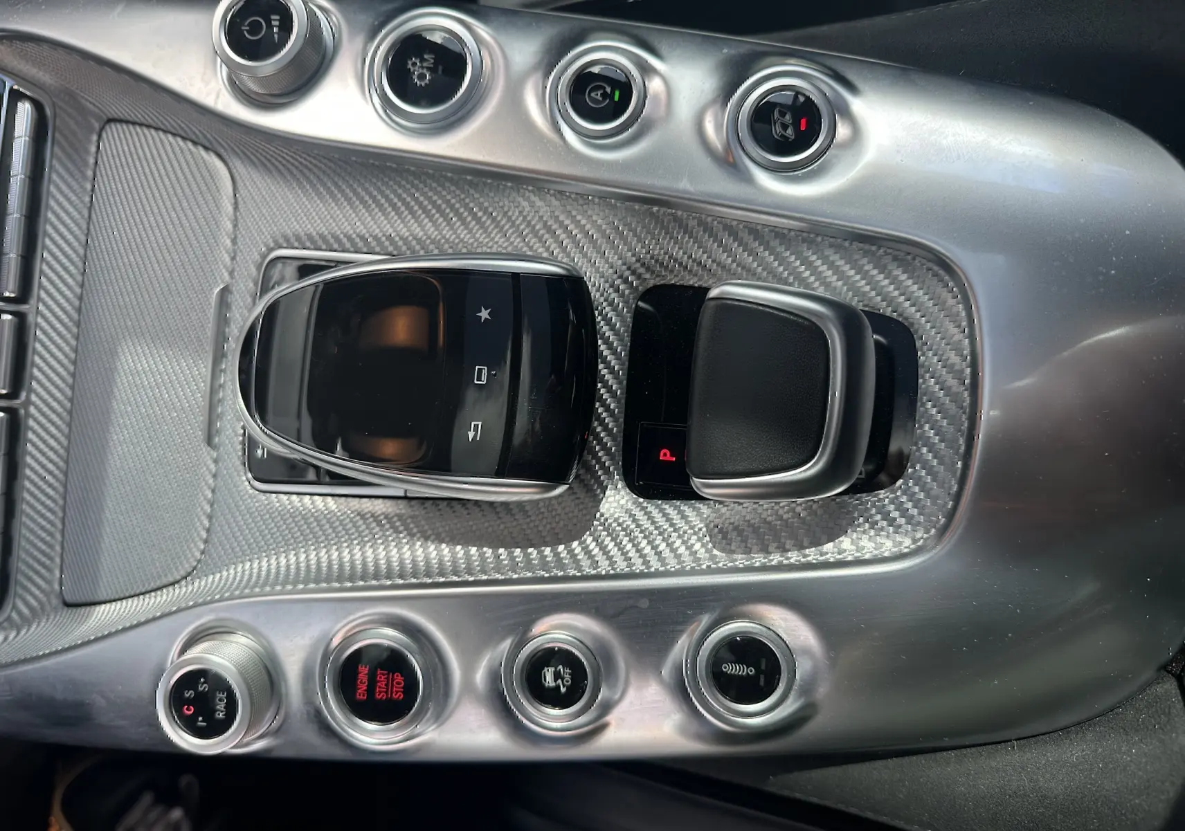 Gros plan sur la console centrale en carbone du Mercedes AMG GT gris foncé, avec commandes et bouton start/stop visibles.