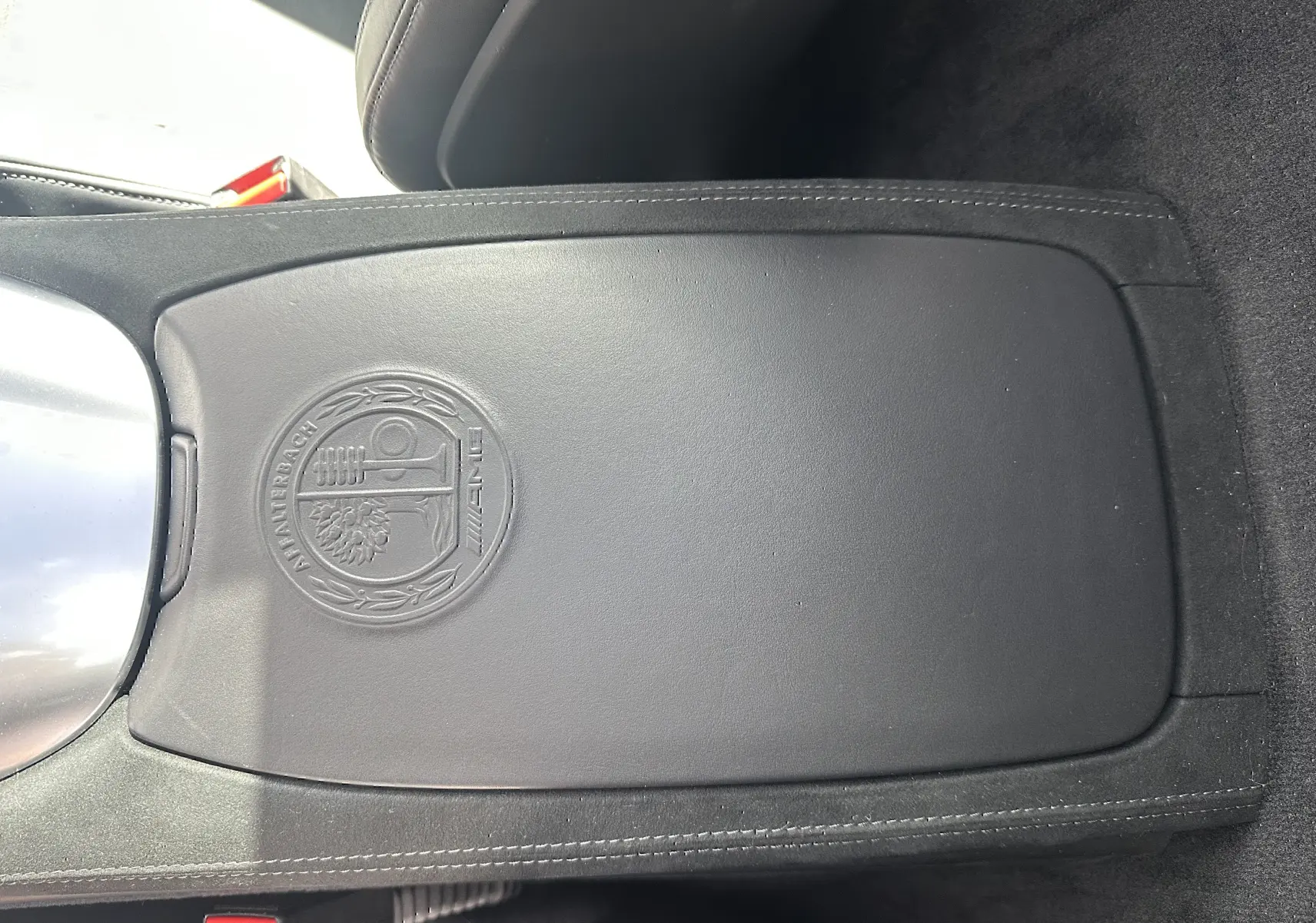 Détail intérieur montrant la console centrale en cuir noir avec logo AMG embossé sur Mercedes AMG GT gris foncé 2015.