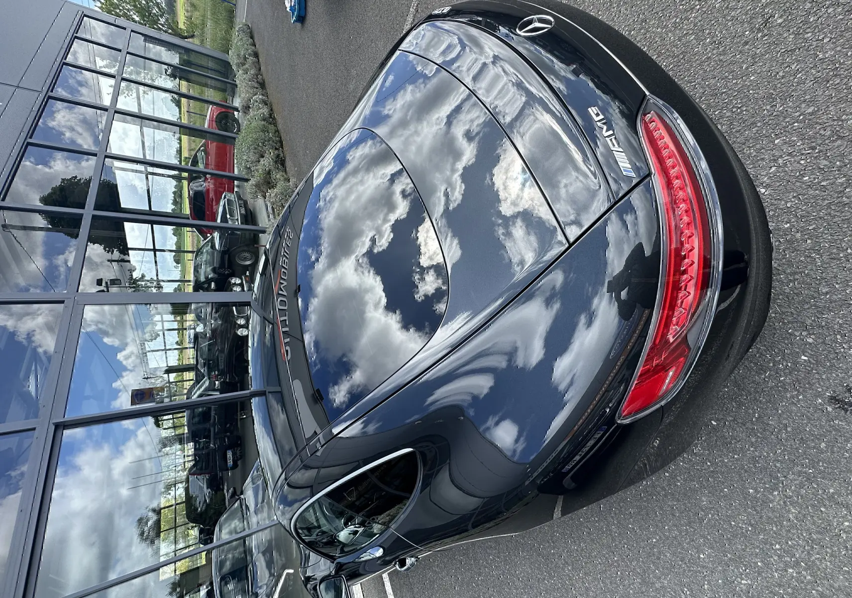 Vue arrière en 3/4 d'une Mercedes AMG GT gris foncé brillant, avec feux arrière allongés et logo AMG visible.