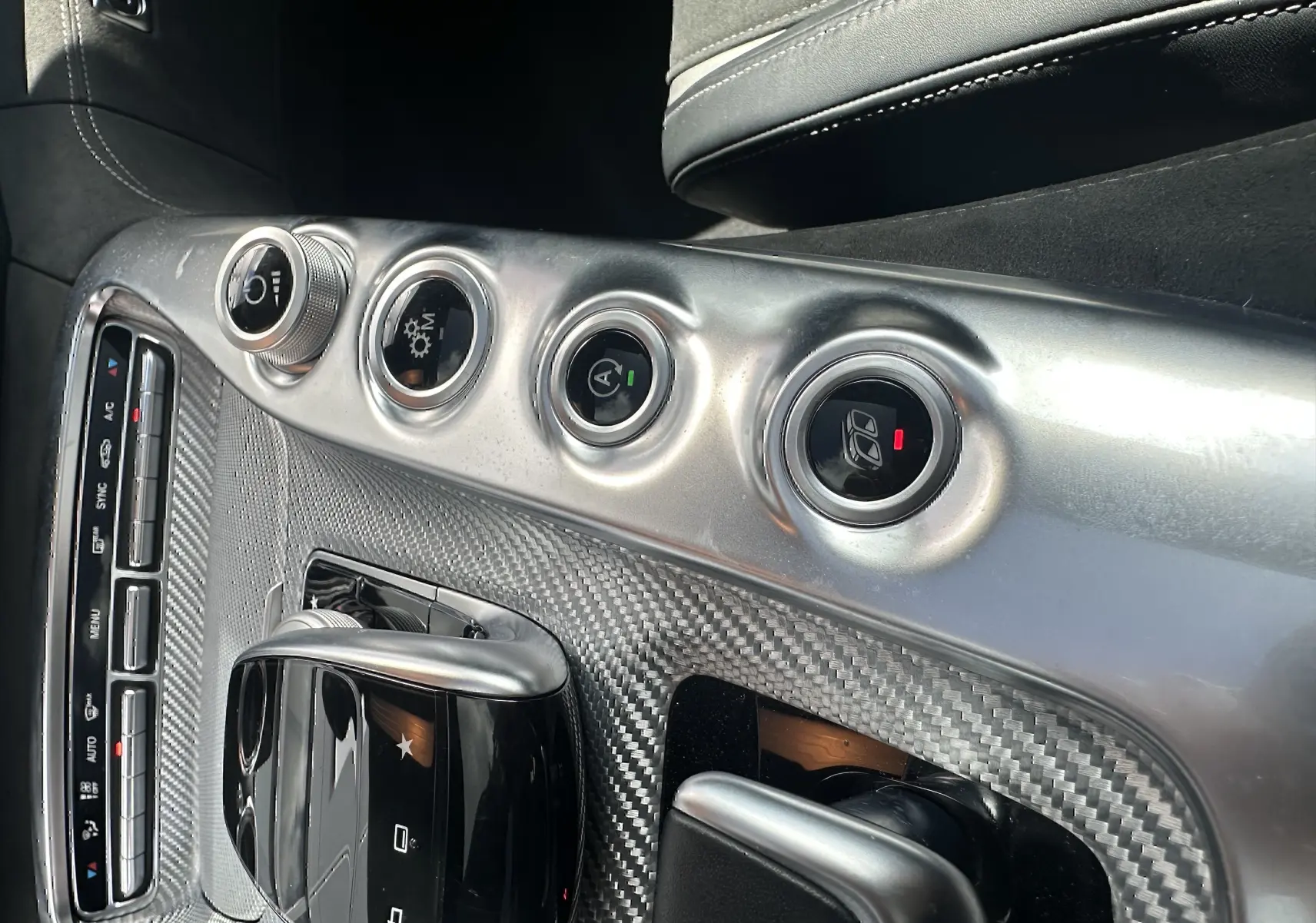 Vue rapprochée de la console centrale en fibre de carbone du Mercedes AMG GT 2015 avec commandes circulaires et pavé tactile noir brillant.