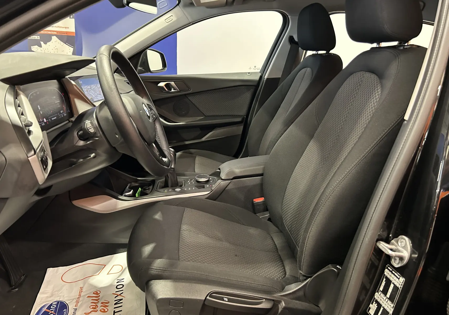 Intérieur noir de la BMW Série 1 16d 2023 vu côté conducteur, avec sièges tissu et tableau de bord moderne.