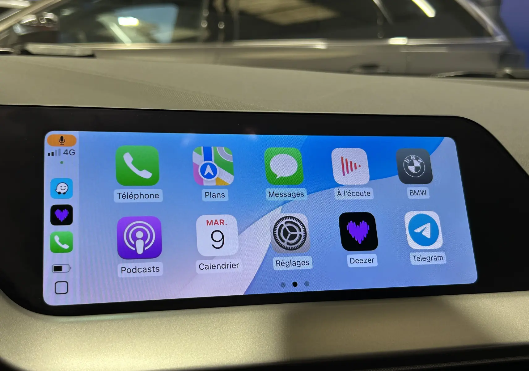 Écran tactile central de la BMW Série 1 16d 2023 affichant les applications Apple CarPlay, avec tableau de bord beige visible.