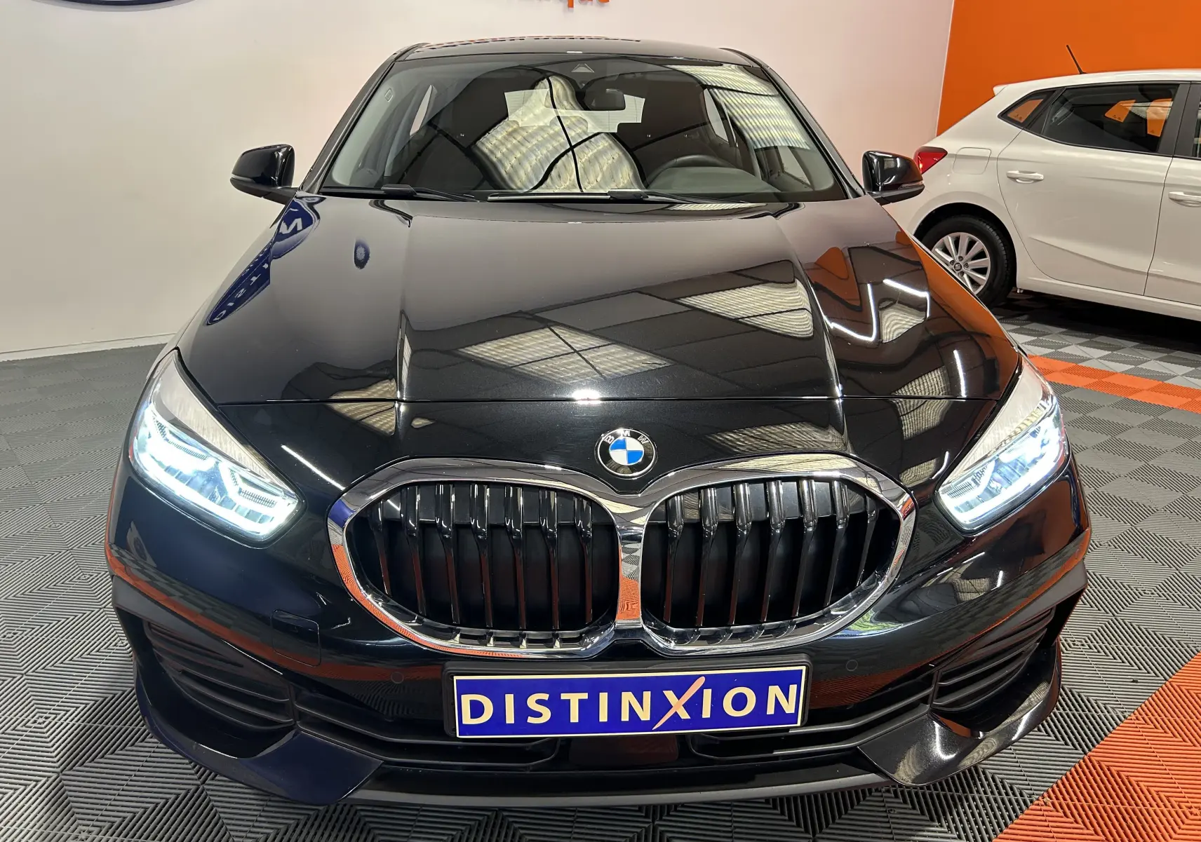 Vue avant d'une BMW Série 1 noire 2023 avec phares LED allumés et calandre caractéristique en double haricot.