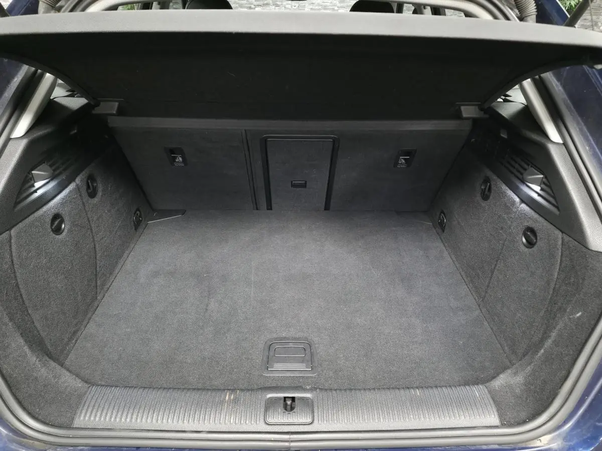 Coffre ouvert en vue arrière d'une Audi A3 Sportback bleu, avec tapis de sol gris et trappe à skis intégrée.