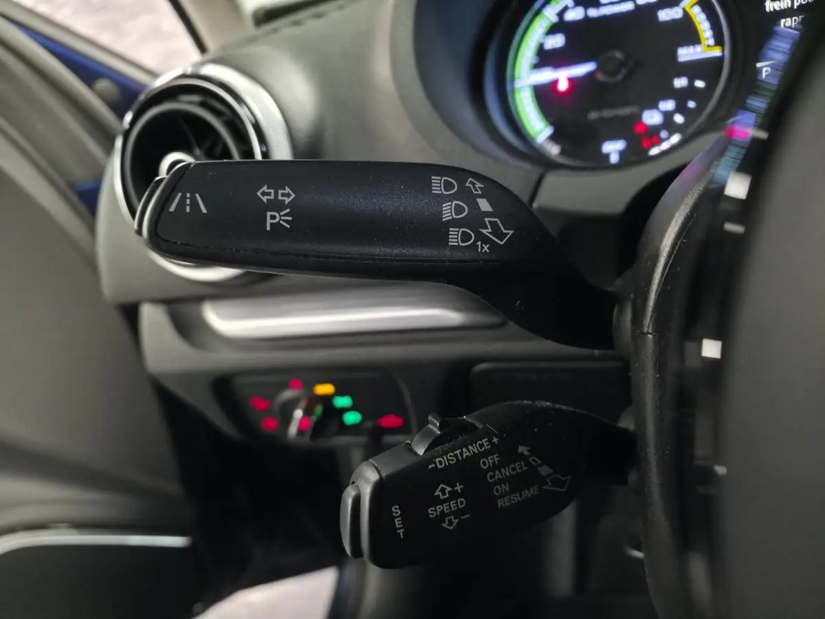 Gros plan sur les commandes au volant côté gauche de l'Audi A3 Sportback bleu, avec indicateurs de feux et régulateur adaptatif.