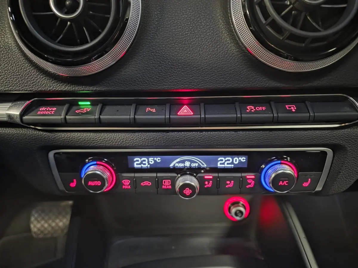 Tableau de bord intérieur de l'Audi A3 Sportback bleu, avec commandes climatisation et boutons éclairés rouges et bleus.