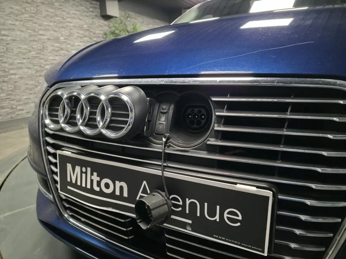 Vue rapprochée avant d'une Audi A3 Sportback bleu avec prise de recharge visible derrière l'emblème Audi ouvert.
