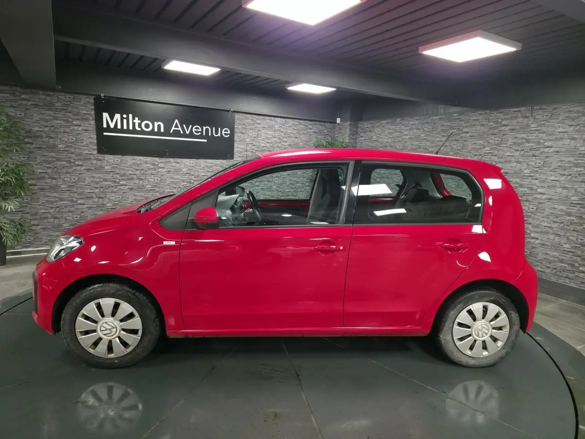 Profil droit d'une Volkswagen Up rouge 2018 avec jantes acier et enjoliveurs VW en aluminium dans un showroom.