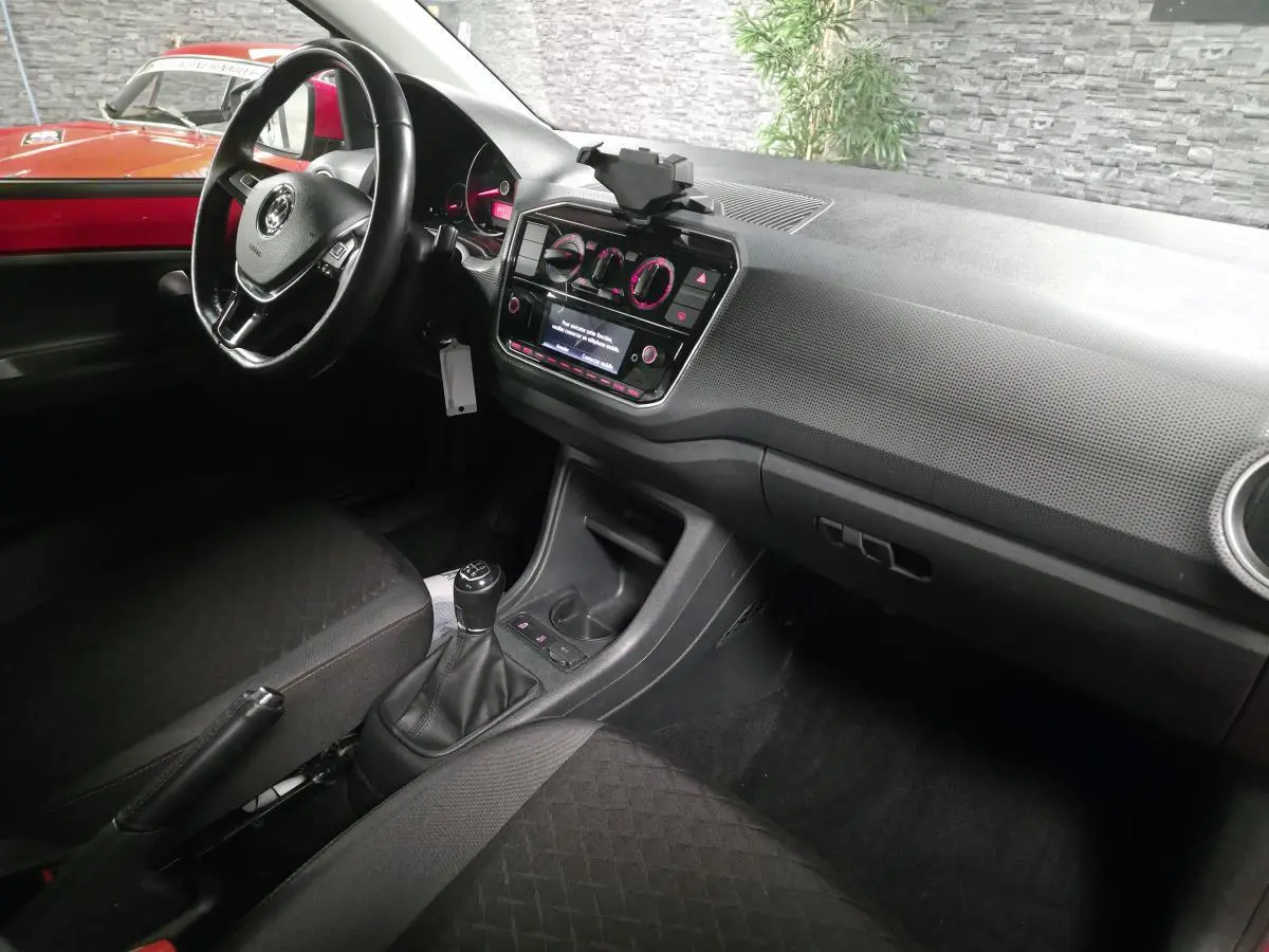 Intérieur avant droit d'une Volkswagen Up rouge, volant cuir multifonctions et levier de vitesses manuel visibles.