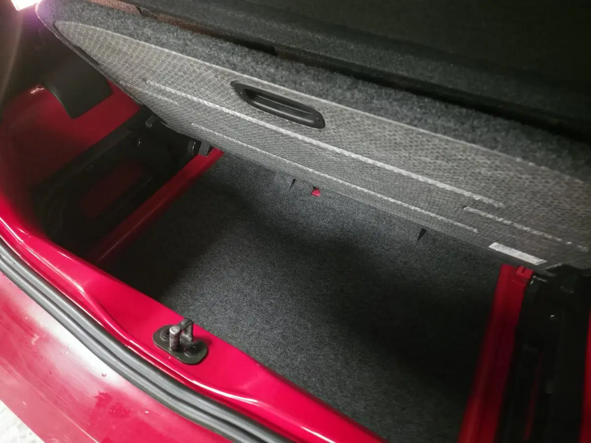 Coffre ouvert vu de dessus d'une Volkswagen Up rouge, montrant le double plancher de chargement en feutre.
