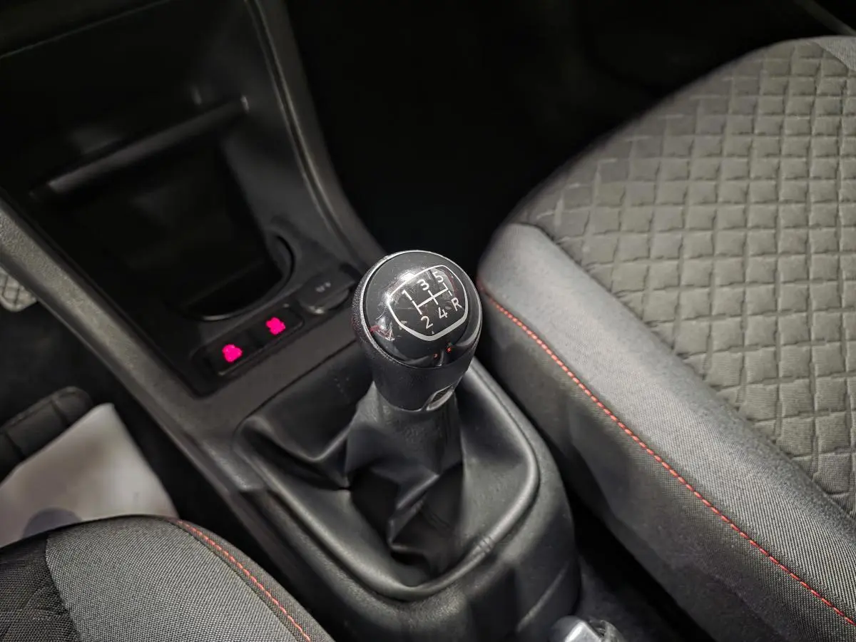 Gros plan sur le levier de vitesses manuel noir et la sellerie grise avec surpiqûres rouges dans une Volkswagen Up rouge.