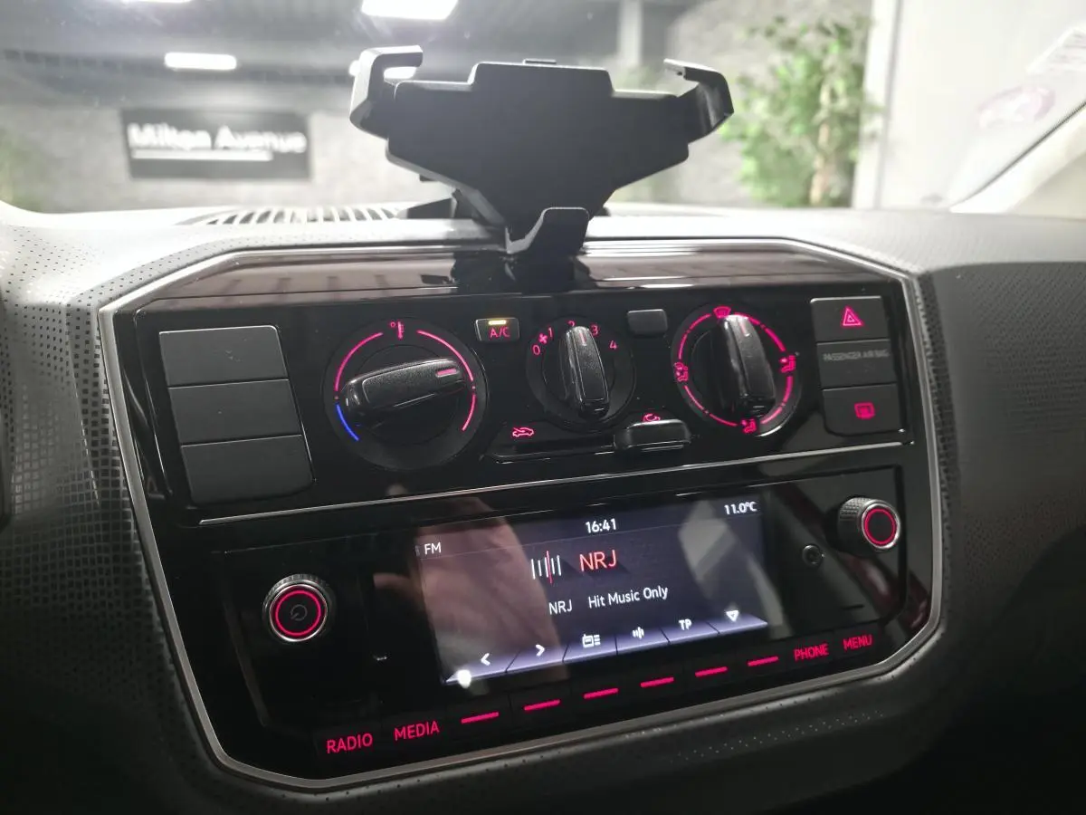 Console centrale avec commandes de climatisation et écran multimédia allumé dans une Volkswagen Up rouge de 2018.