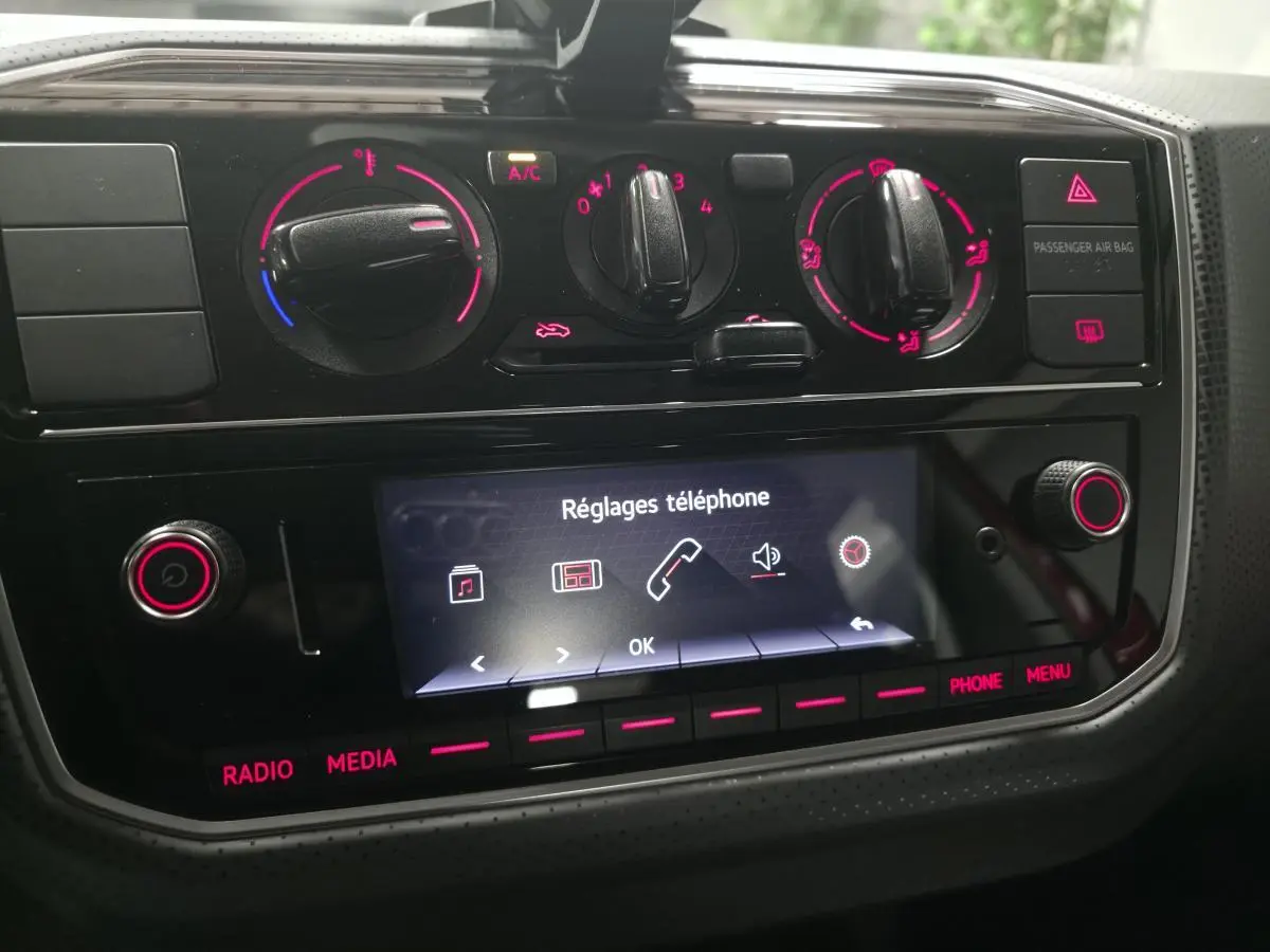 Tableau de bord de Volkswagen UP rouge 2018, vue rapprochée sur commandes climatisation et écran tactile réglages téléphone.