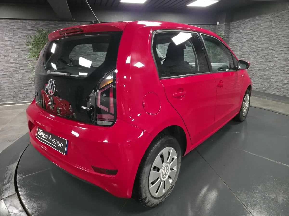 Volkswagen Up rouge vue 3/4 arrière droit avec jantes acier et vitre arrière teintée dans un showroom.