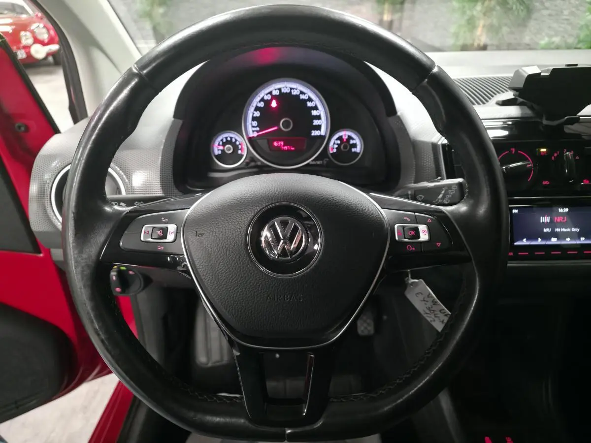 Vue intérieure centrée sur le volant cuir multifonctions d'une Volkswagen Up rouge, avec tableau de bord éclairé.
