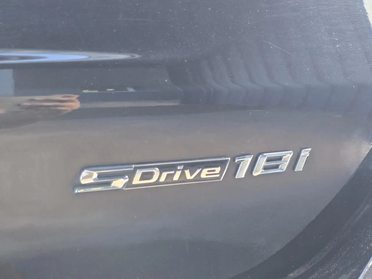 Gros plan sur l'emblème sDrive18i argenté sur la carrosserie noir saphir métallisé d'un BMW X1 F48.