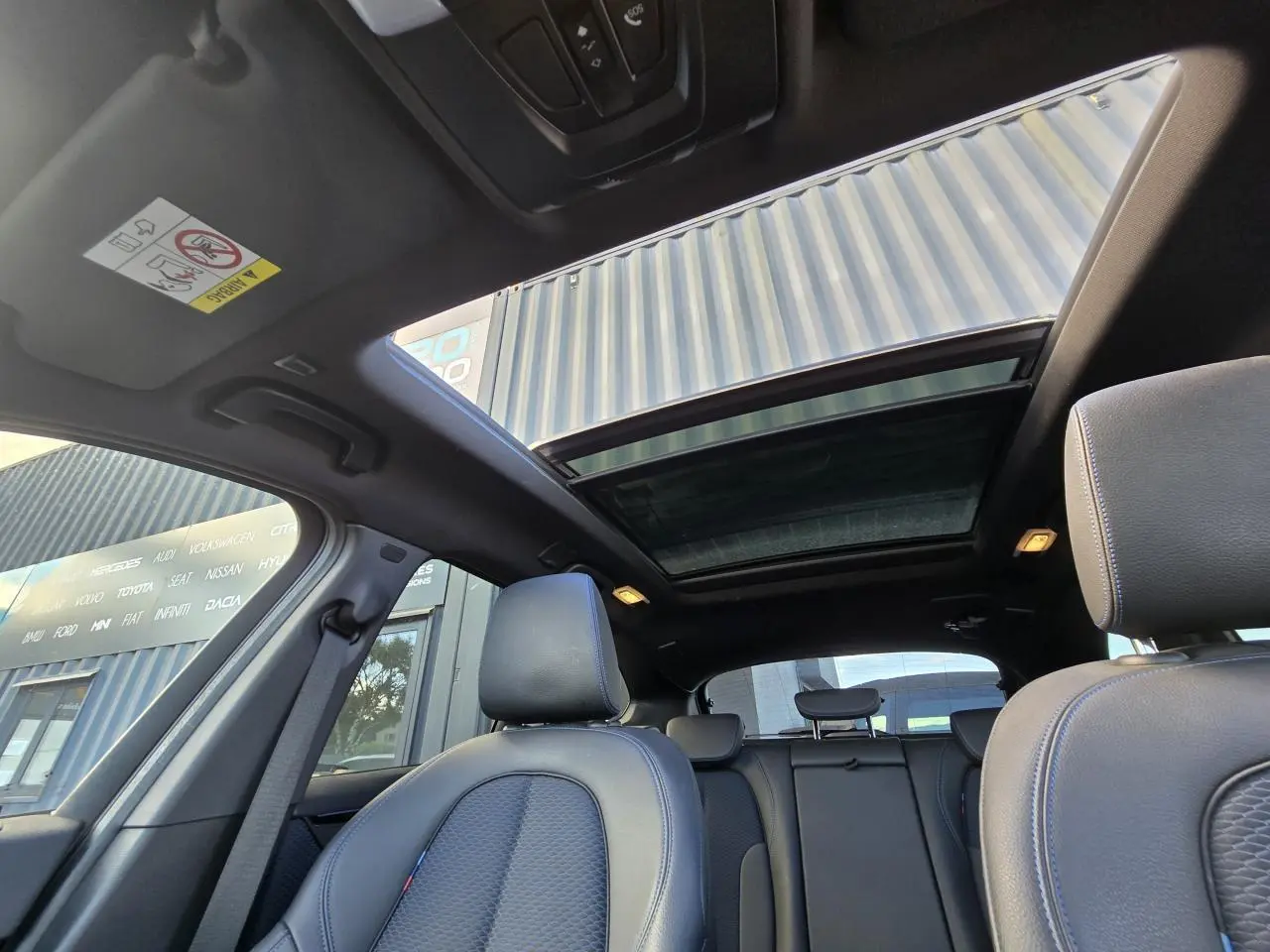 Vue intérieure du toit ouvrant panoramique et des sièges avant en tissu noir du BMW X1 F48 noir saphir métal.