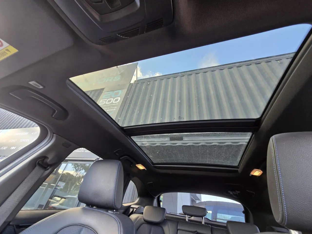 Toit ouvrant panoramique vu de l'intérieur arrière du BMW X1 noir Saphir Metal avec sièges en tissu noir et surpiqûres bleues