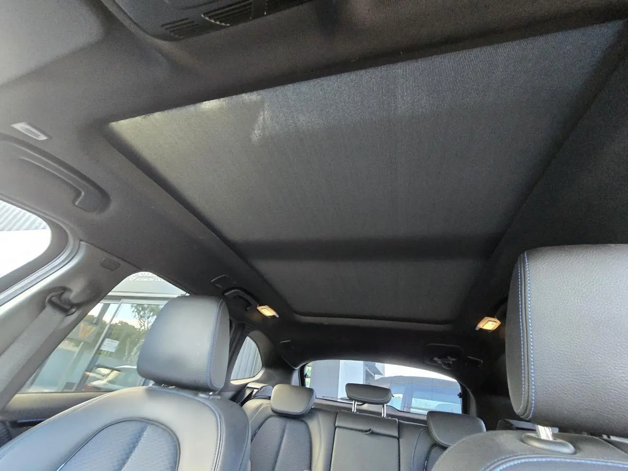 Vue intérieure du toit ouvrant panoramique et des sièges noirs avec surpiqûres bleues d'un BMW X1 F48 M Sport 2020.