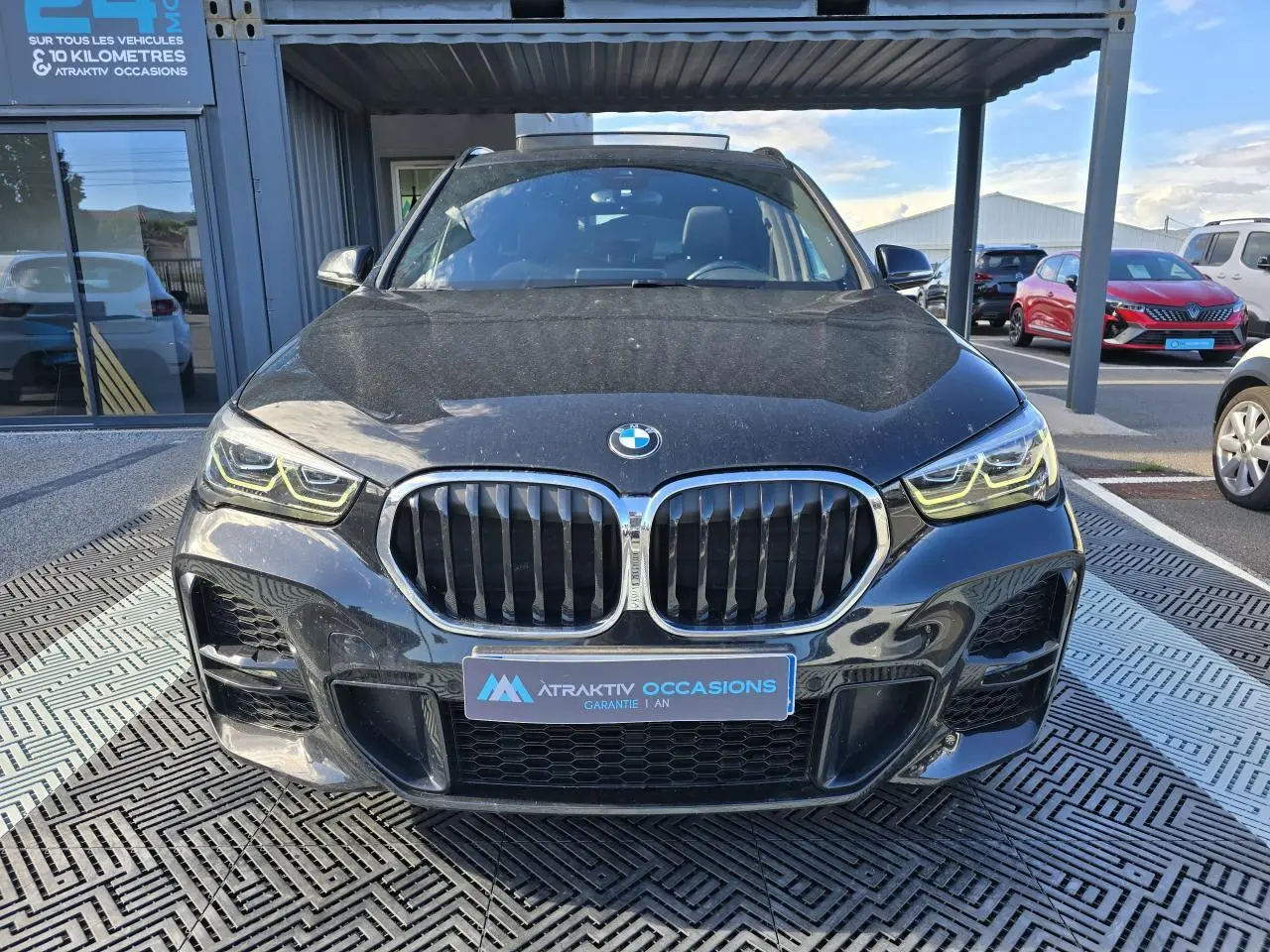 Vue frontale d'un BMW X1 noir saphir métallisé avec calandre double haricot et phares LED allumés.