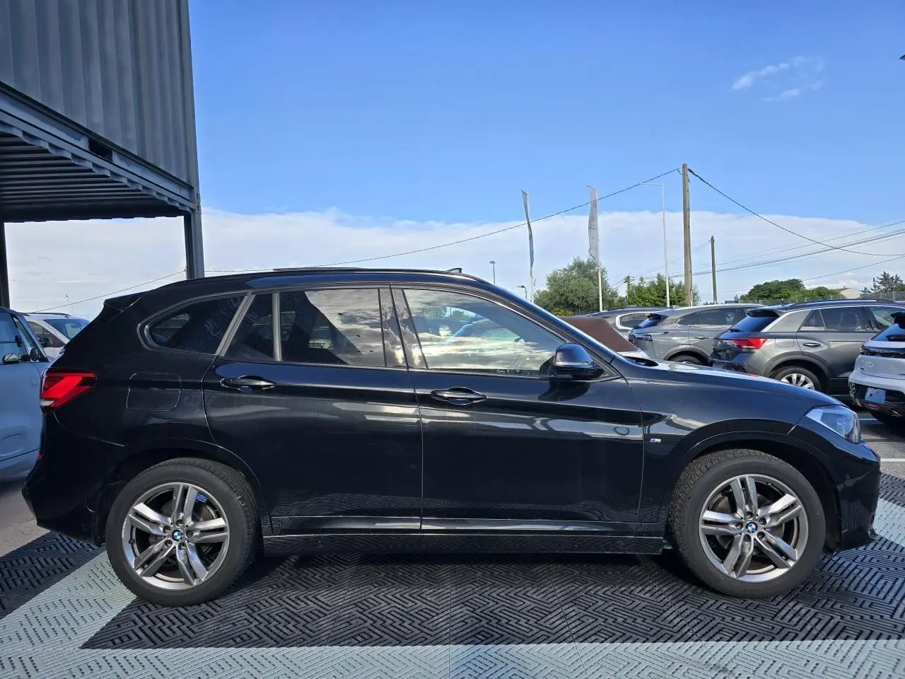 Profil côté gauche d'un BMW X1 noir saphir métallisé avec jantes alliage 18 pouces et badge M Sport visible.