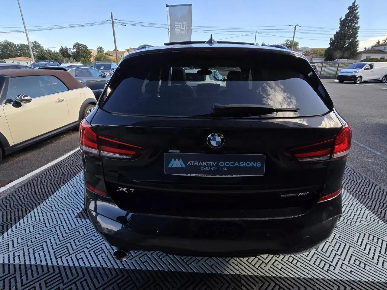 Vue arrière d'un BMW X1 noir saphir métallisé avec feux arrière LED et sortie d'échappement chromée à gauche.