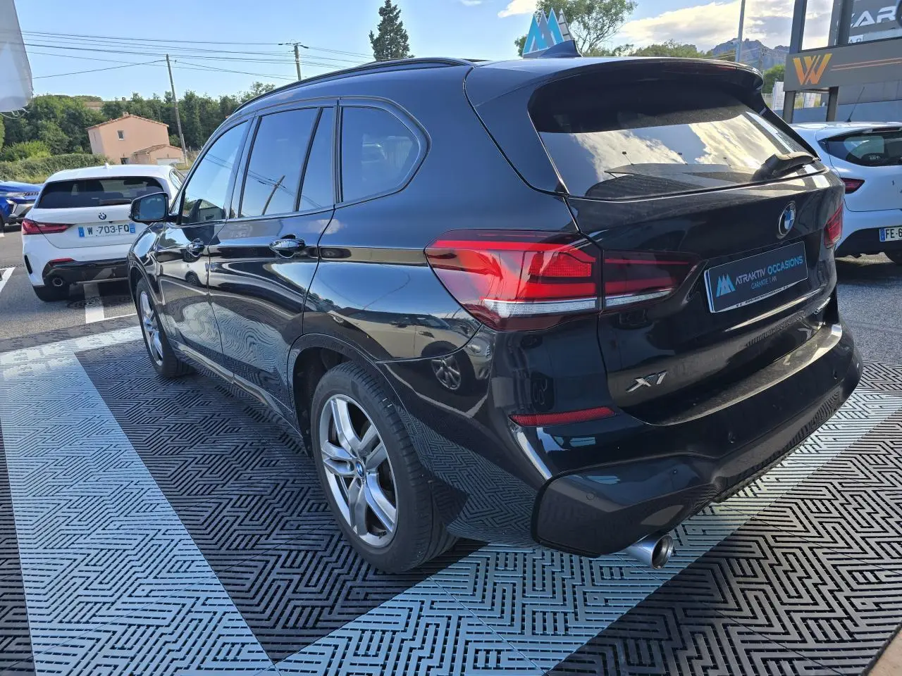 BMW X1 noir saphir métal vue 3/4 arrière droit, avec sortie d'échappement chromée et vitres teintées.