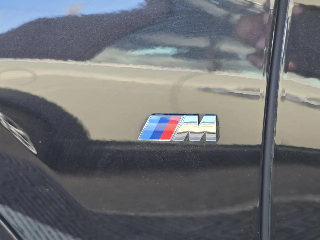 Gros plan sur l'emblème M tricolore sur la porte latérale gauche d'un BMW X1 noir saphir métallisé.
