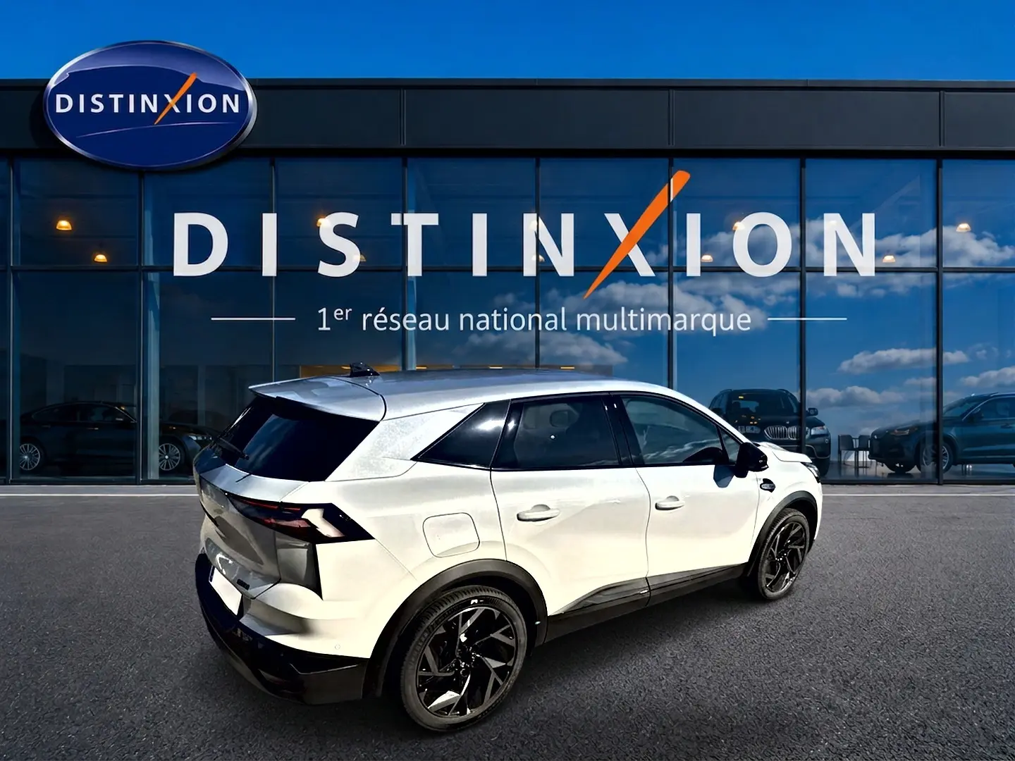 Vue 3/4 arrière droite du Renault Symbioz blanc nacré avec jantes noires devant une vitrine Distinxion.
