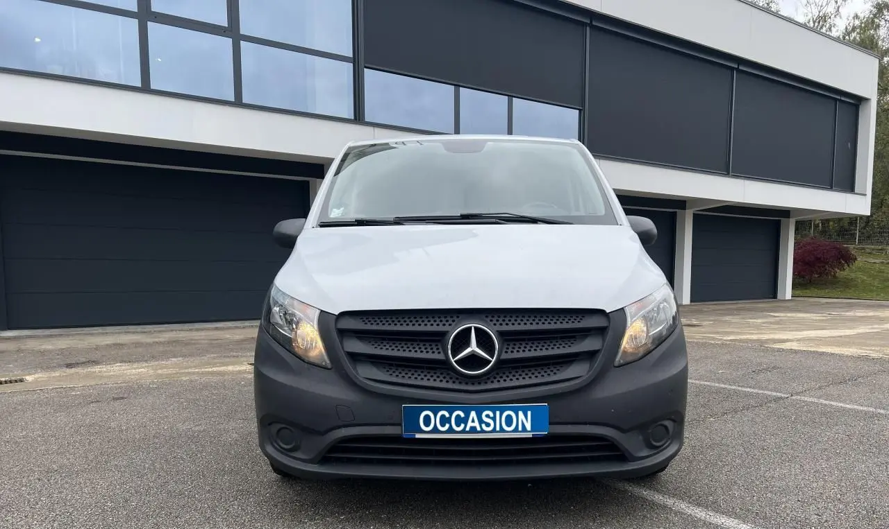 Vue frontale d’un Mercedes Vito Fourgon blanc avec calandre noire et plaque « OCCASION » en extérieur devant un bâtiment moderne.