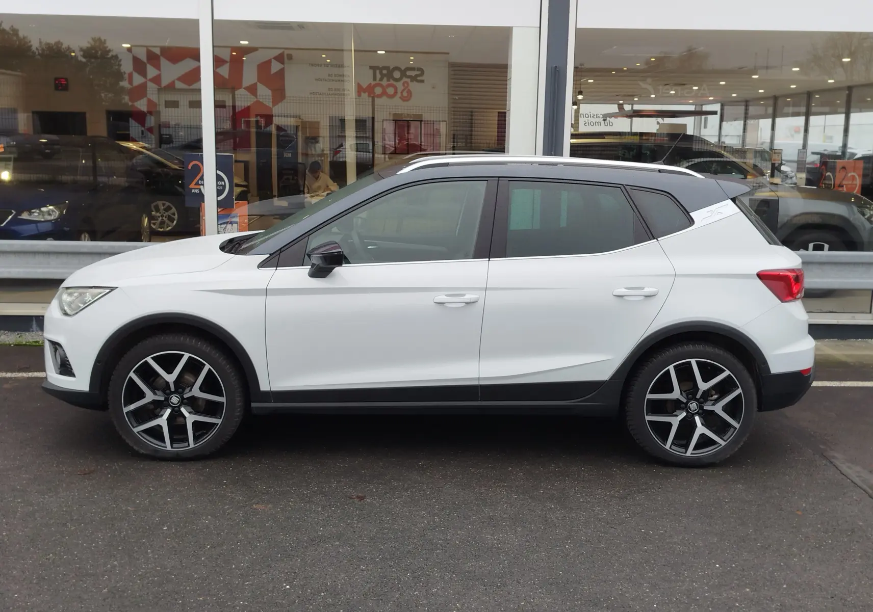 Vue de profil côté gauche d'un SEAT Arona blanc avec toit gris magnétique et jantes alliage noires et argentées.